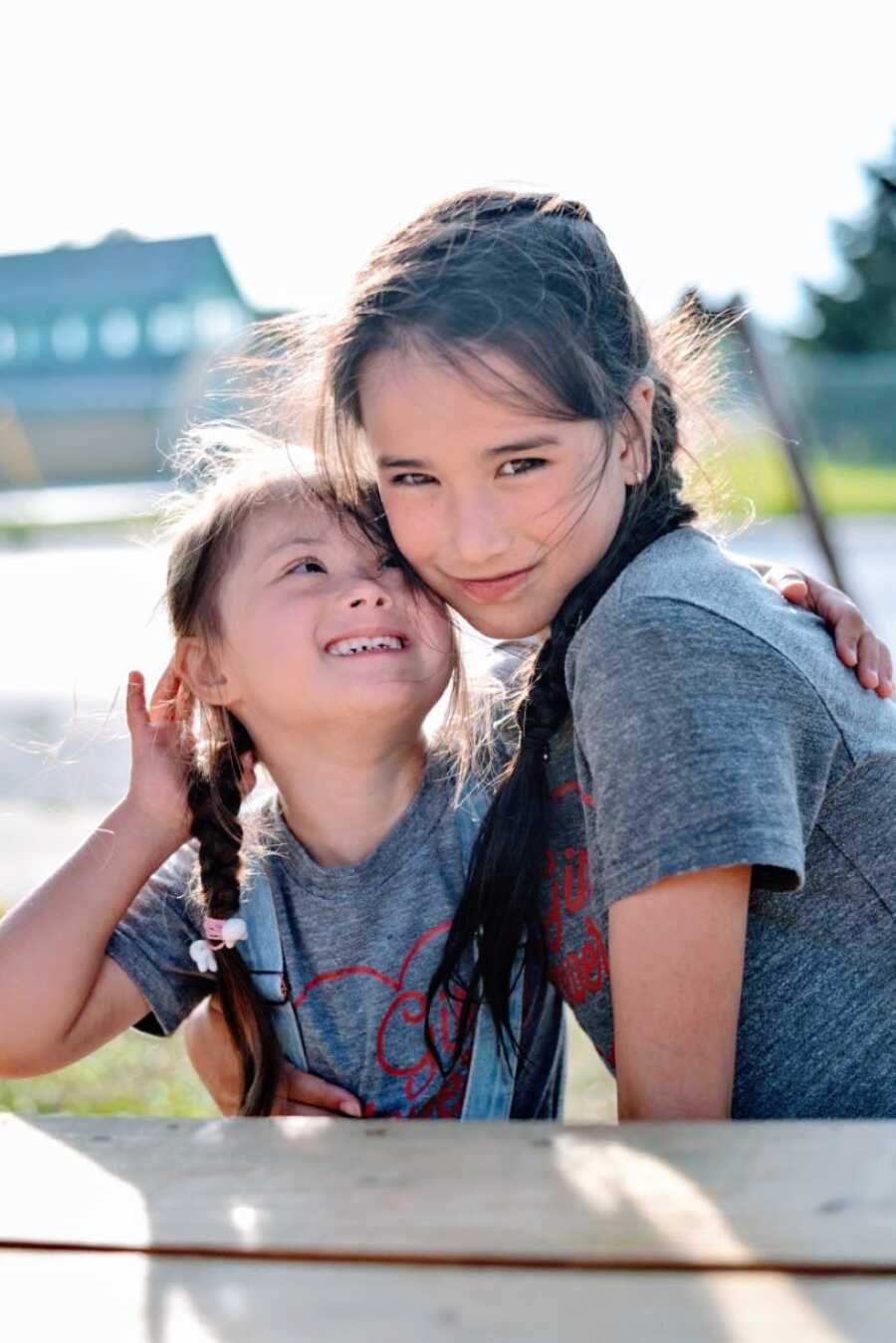 Two sisters wearing matching shirts with matching braids smile for a photo together